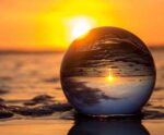 Crystal ball on the beach reflecting a vibrant ocean sunset scene