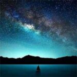 A small sailboat glides across a calm lake under a breathtaking Milky Way sky, surrounded by distant mountain silhouettes.