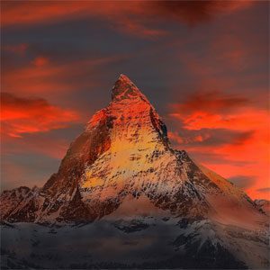 A dramatic snow-capped mountain peak glowing with fiery hues under a sunset sky