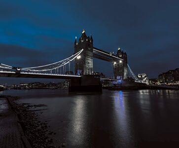 Tower Bridge in London lit up at night with reflections shimmering on the River Thames