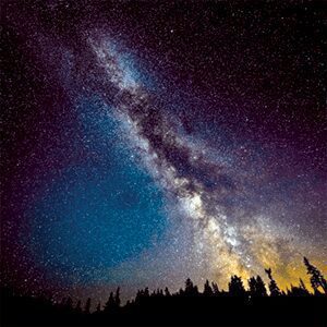 A silhouetted group of people gazes up at a spectacular Milky Way band stretching across a deep purple and blue night sky.
