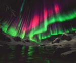 Green and pink aurora borealis streak across the night sky above snowy arctic terrain, reflecting vibrantly in icy waters below.