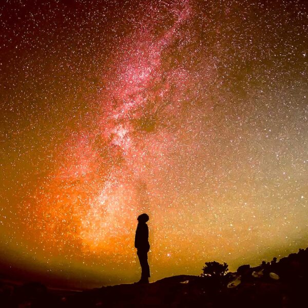 Silhouette of a person standing under a vivid red-orange aurora borealis sky filled with stars