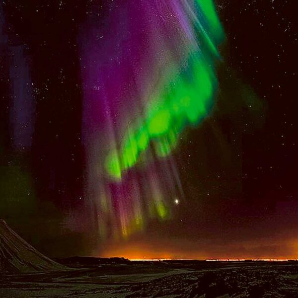 Vibrant aurora borealis with streaks of green and purple lighting up a starry sky above a mountainous horizon