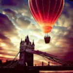 A hot air balloon soaring above Tower Bridge in London, captured in a vibrant sunset glow, perfectly displayed in a LED Box Frame to enhance your space.