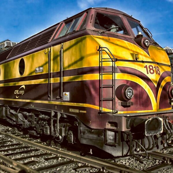 A vintage yellow and burgundy diesel locomotive labeled 1818, stationed on railway tracks under a bright blue sky.