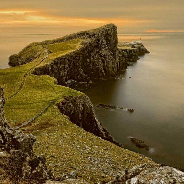 A dramatic cliffside view in Scotland with winding paths and a lighthouse at dusk