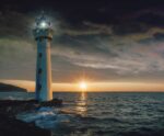 A lighthouse glowing at twilight with the sun setting over the ocean horizon and waves gently crashing below