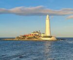 St Mary’s Lighthouse in Newcastle illuminated by golden hour sunlight, standing on a rocky coastal island surrounded by calm sea